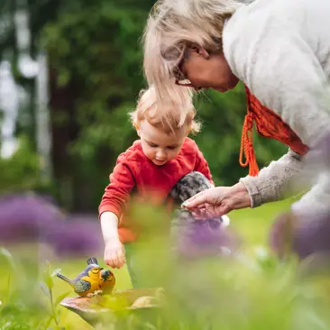 Elderly lady interacts with a young child in a garden.