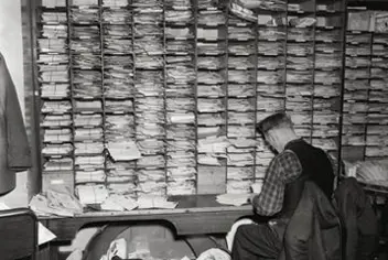 An old photograph showing a man sitting at a desk, sorting documents